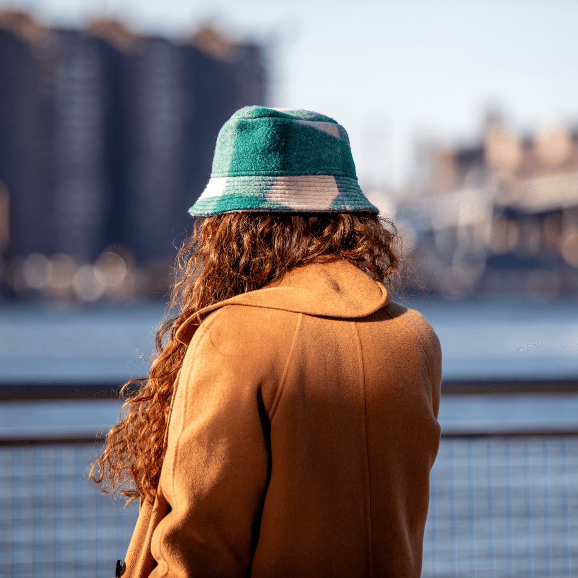 Woman wearing a hat and looking out at the East River, near Williamsburg Wharf.